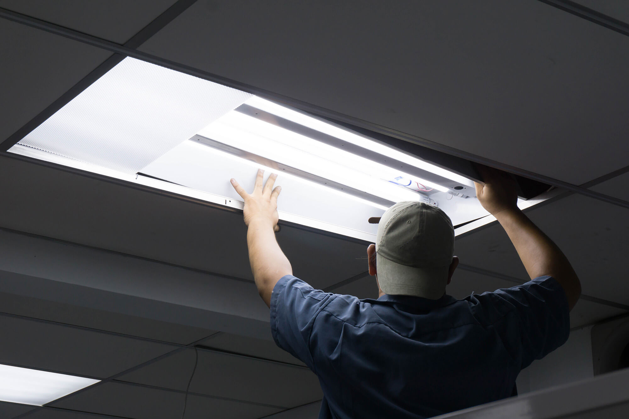 Electrician checking fluorescent light tube in office building